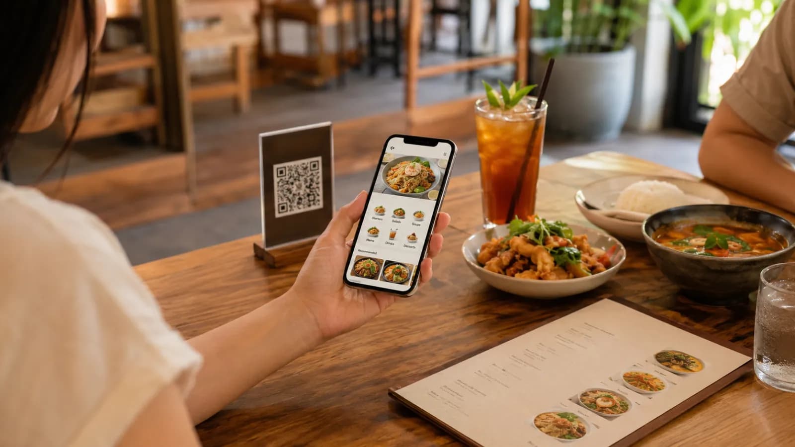 Restaurant guests reading a view-only digital menu on a phone beside a QR table card and printed backup menu.